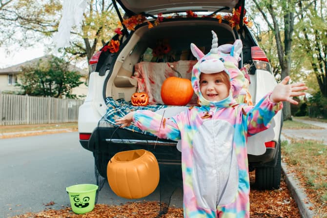 child in a unicorn costume in front of an SUV with its trunk open