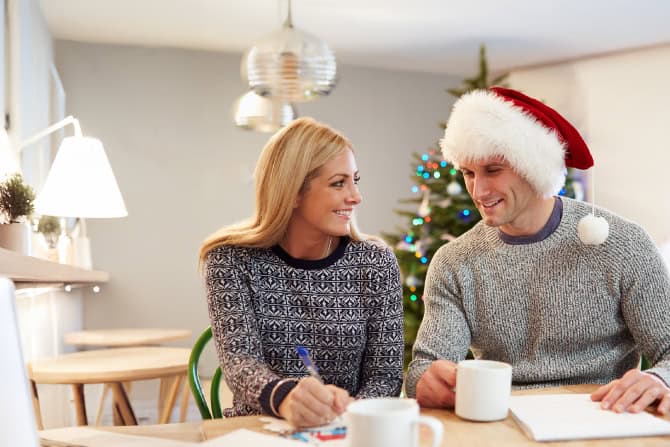 man with santa hat and woman sitting at a table with coffee mugs and pad of paper