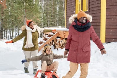 a dad pulling his son in a sled with the mom smiling behind them