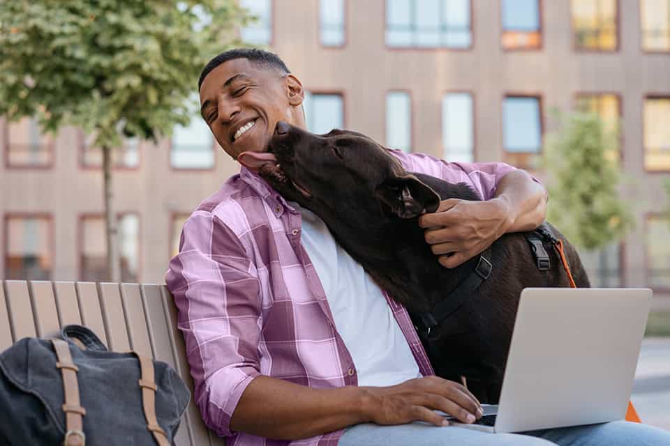 man holding dog smiling and on laptop